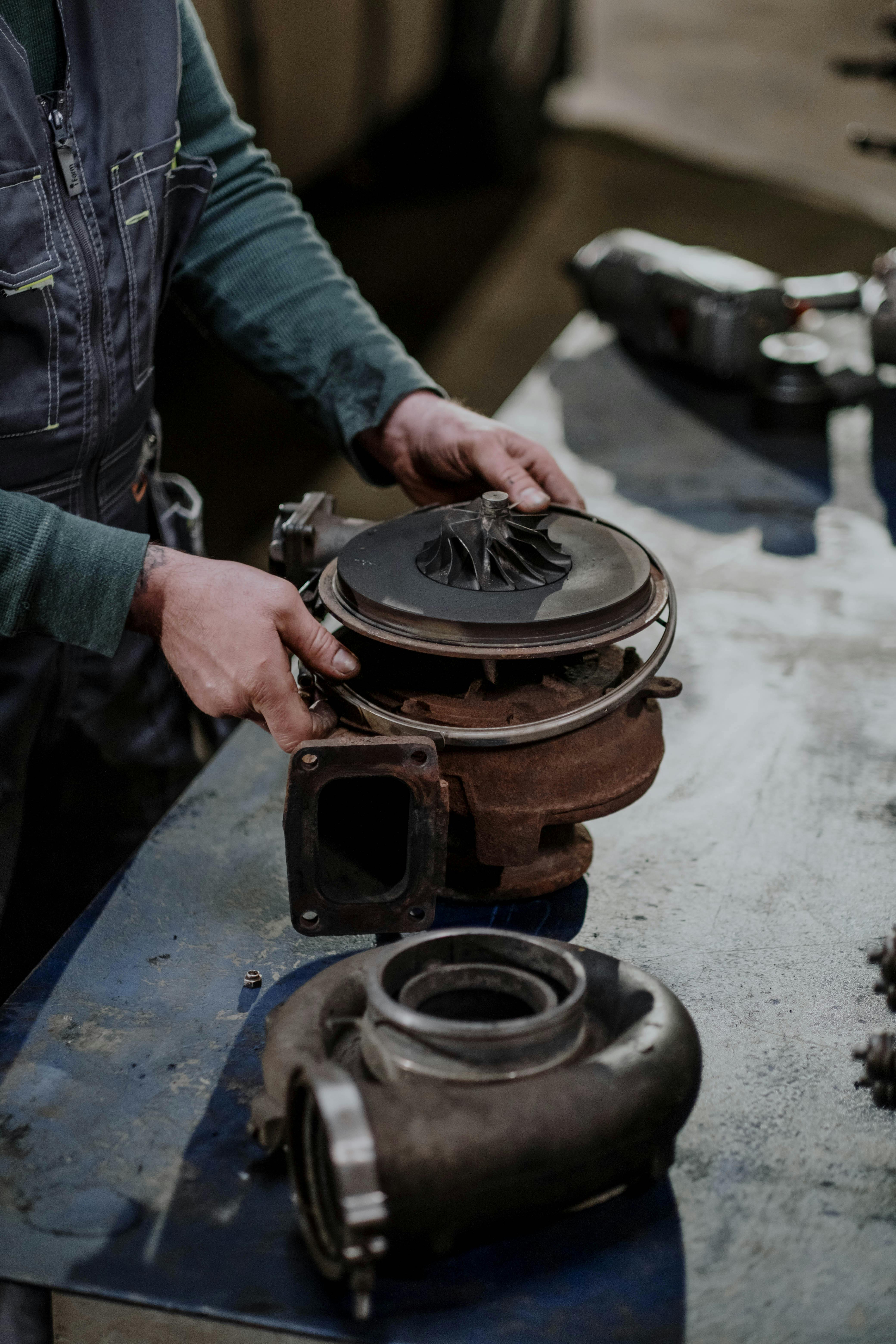 Mechanic working on a turbocharger assembly in a repair shop setting.